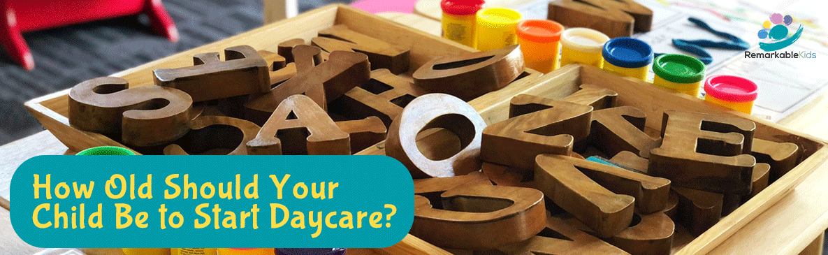 A wooden tray filled with large wooden alphabet letters and several small tubs of colorful play-doh, representing early learning activities.